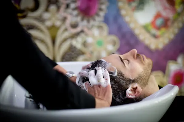 Ein Friseur wäscht einem Mann im Salon professionell die Haare mit Shampoo.